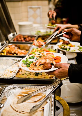 A group of people filling their plates with the food from a catering set up.