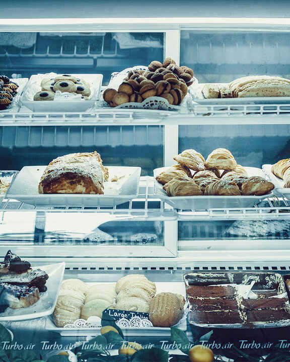 A multi-tiered display case filled with a variety of Italian cookies, Biscotti, and coke desserts