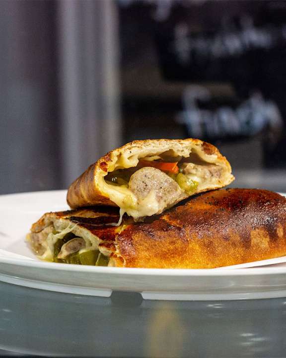 A Italian sausage and pepper Stromboli cut into two pieces, one laying on top of the other 