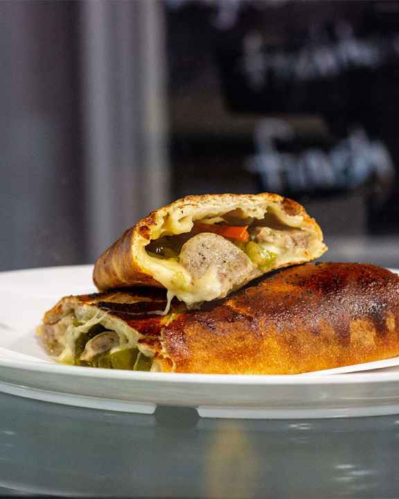 A Italian sausage and pepper Stromboli cut into two pieces, one laying on top of the other