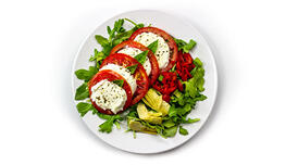 An Arugula Salad with large slices of tomatoes and mozzarella